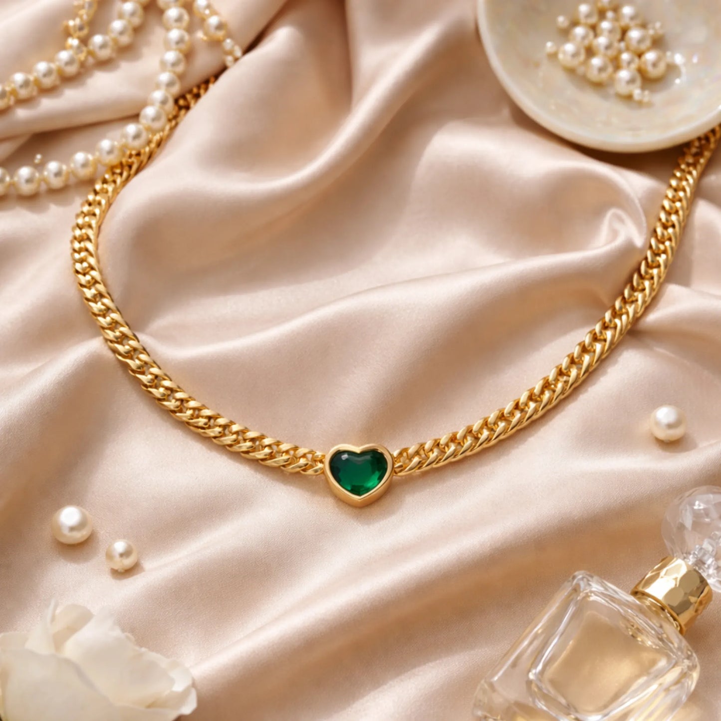 Gold chain necklace with a green heart pendant on a beige fabric background.