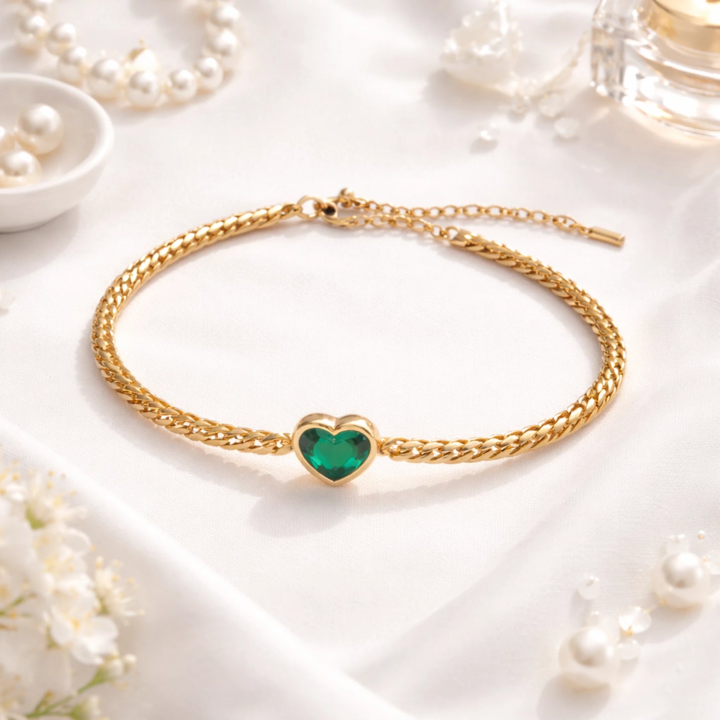 Gold bracelet with a green heart charm on a white background with pearls and flowers.