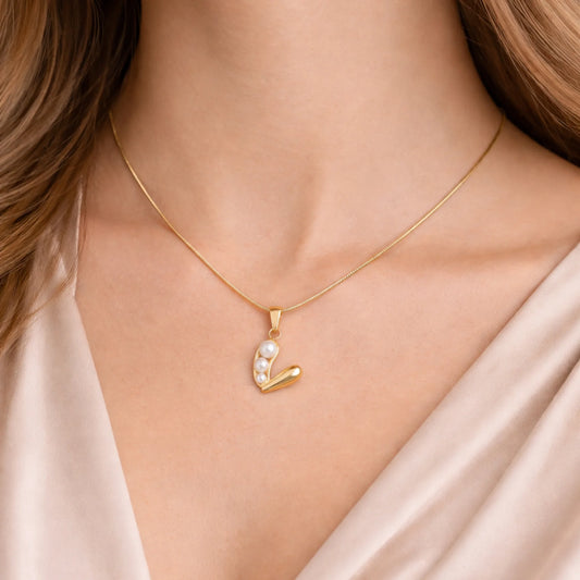 Gold necklace with a pendant featuring pearls on a person wearing a beige top.