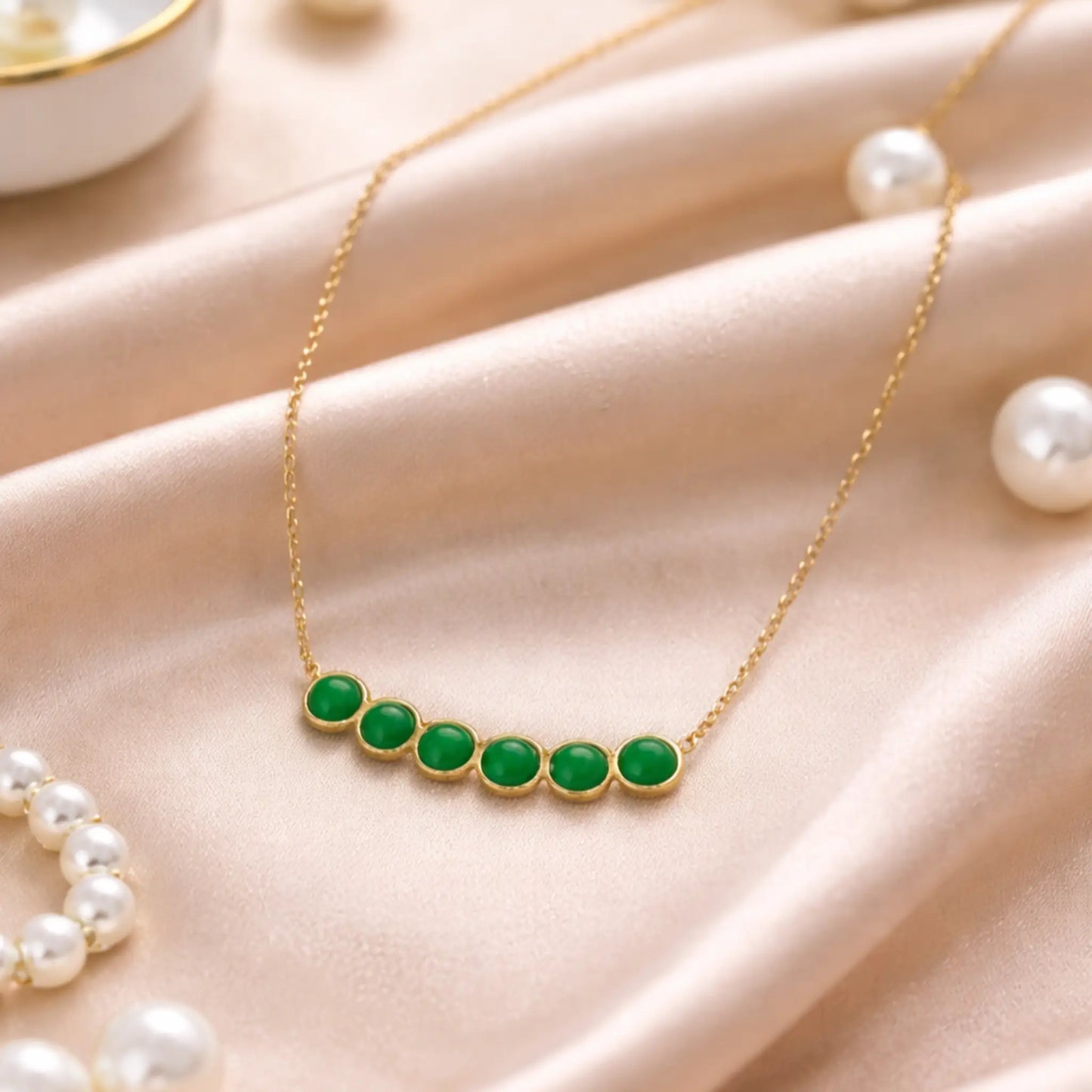 Gold necklace with green stones on a beige surface