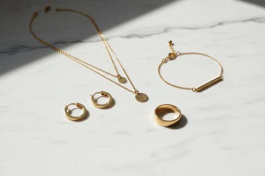 316L stainless steel jewellery with 18K gold PVD finish — earrings, necklace, bracelet and ring flat lay on white marble | YUBIRAA