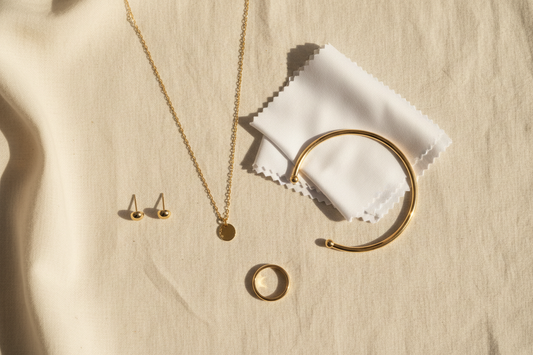 Gold jewellery care flat lay — necklace, earrings, bracelet and ring on ivory linen with soft cloth — YUBIRAA jewellery care guide