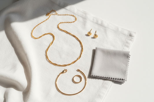 Gold anti-tarnish jewellery flat lay with cleaning cloth — necklace, earrings, bracelet and ring on white linen | YUBIRAA