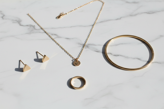  Gold-toned 316L stainless steel jewellery flat lay on white marble — studs, necklace, bracelet and ring by YUBIRAA, is stainless steel jewellery good for daily wear guide
