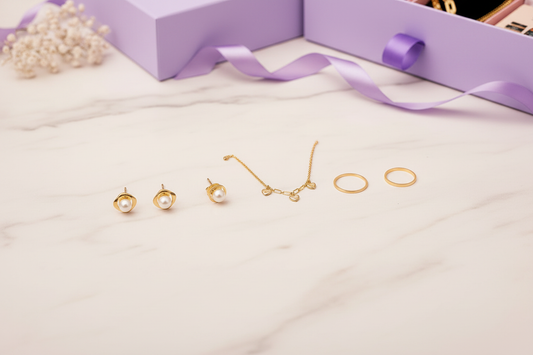 YUBIRAA jewellery hamper guide — gold-toned earrings, necklace, bracelet and ring flatlay with luxury lavender gift box, showing how to build a personalised jewellery hamper
