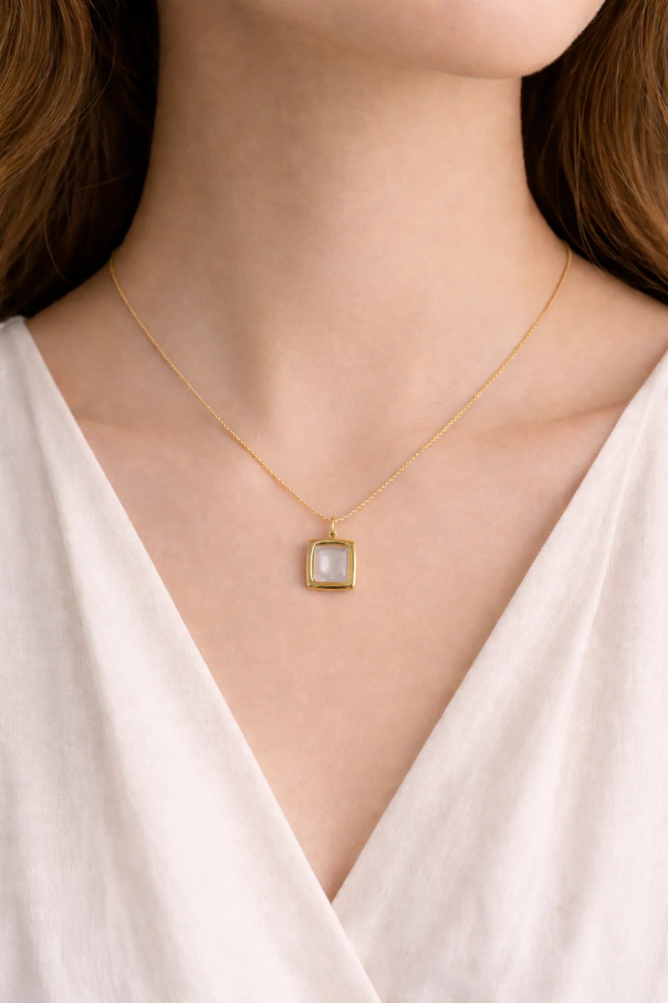 Gold necklace with a square pendant worn by a person in a white top