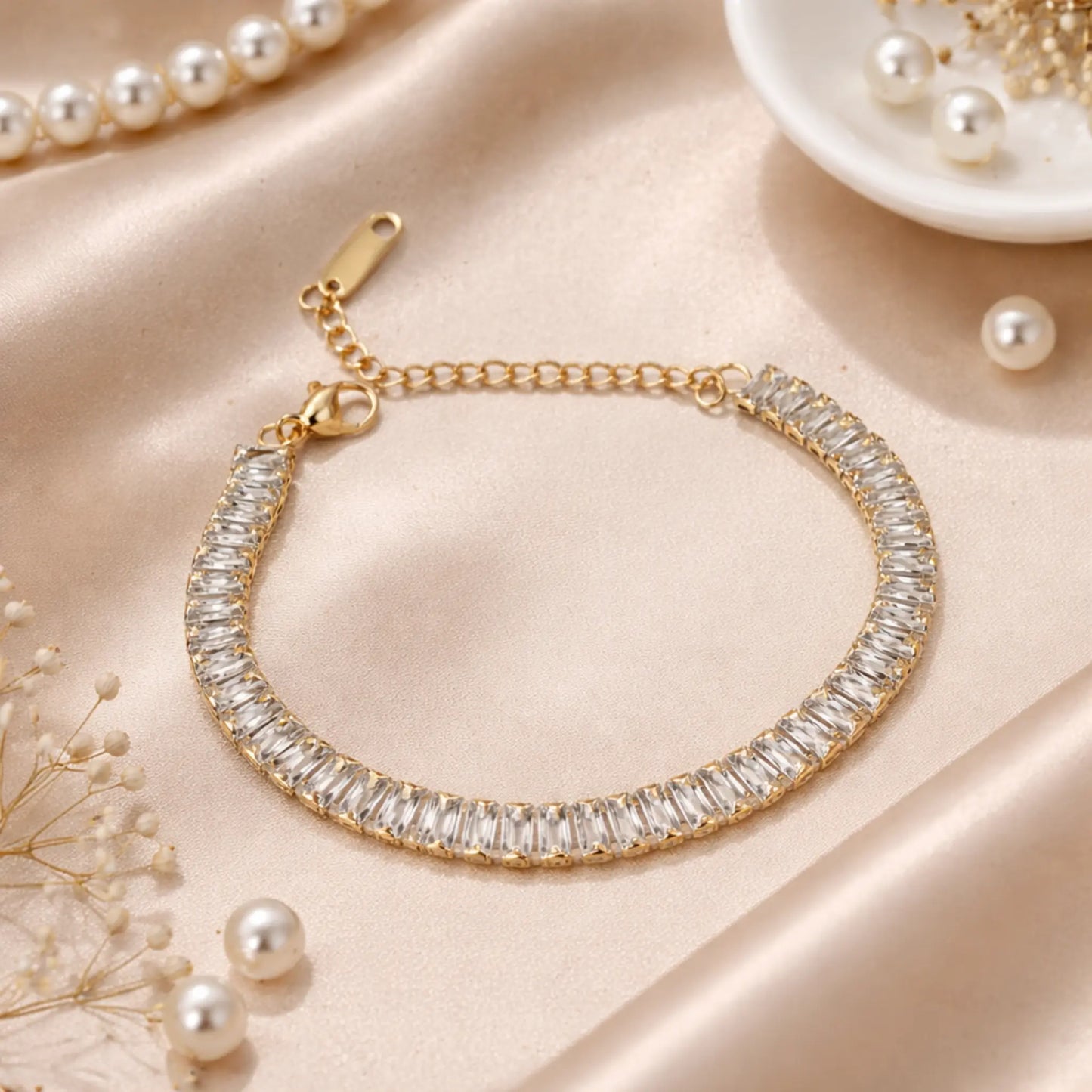 Gold bracelet with clear stones on a beige surface with pearls and jewelry.