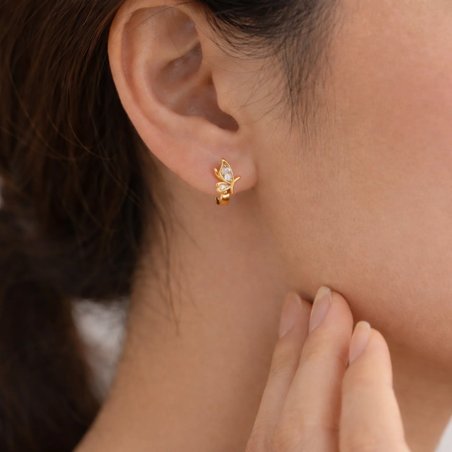 Butterfly gold huggie earrings with marquise stone worn on ear close up