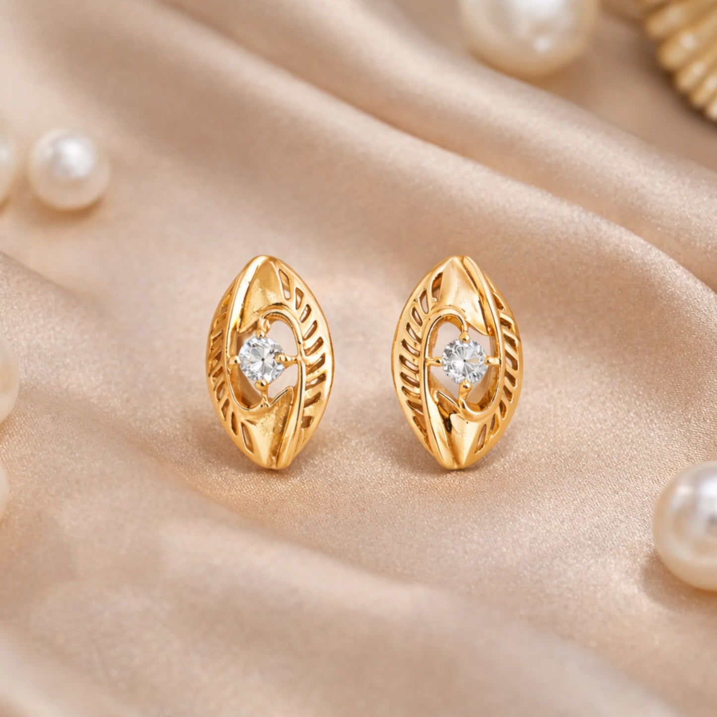 Celeste Marquise gold earrings styled on satin fabric with pearl accents