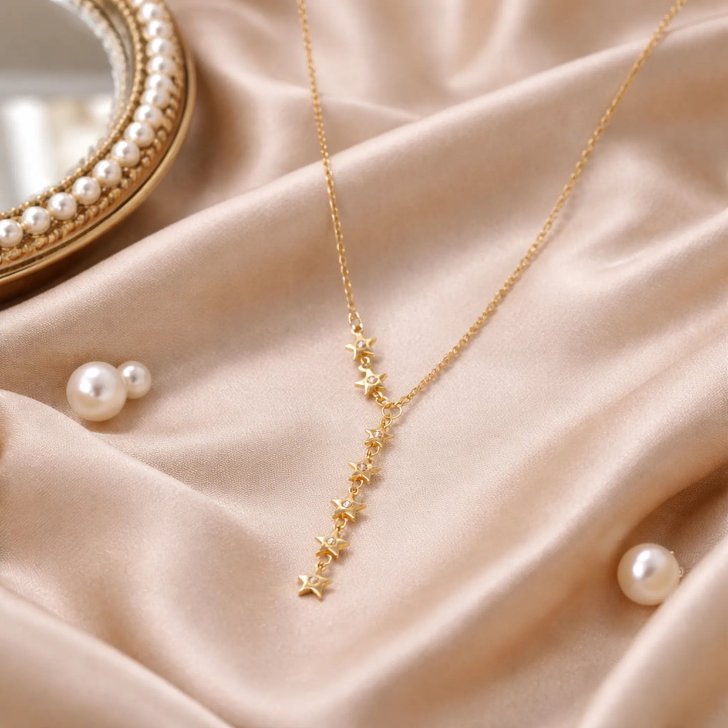 Yubiraa anti tarnish gold star drop necklace styled on satin cloth with pearls in luxury aesthetic