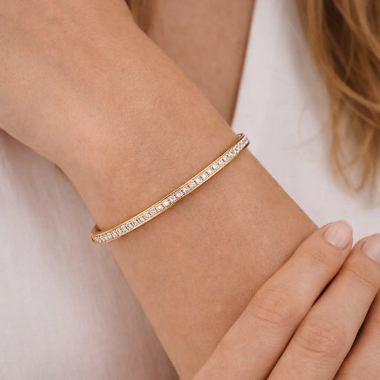 Gold bracelet with clear stones on a wrist against a neutral background