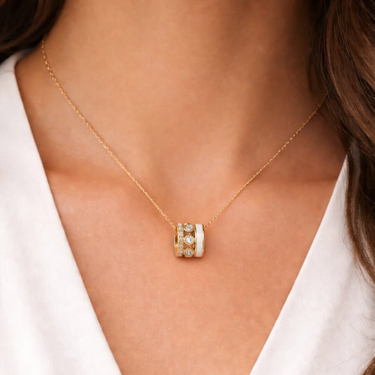 Gold necklace with a cylindrical pendant worn by a person against a neutral background