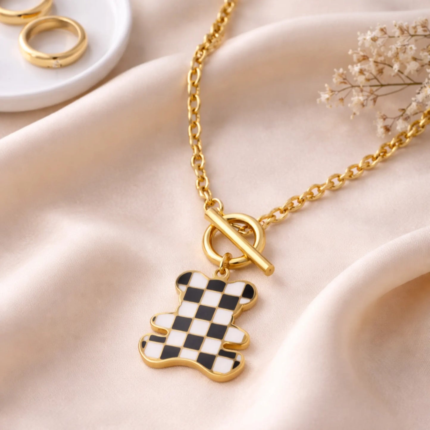 Gold chain necklace with checker teddy charm displayed on Saturn cloth 