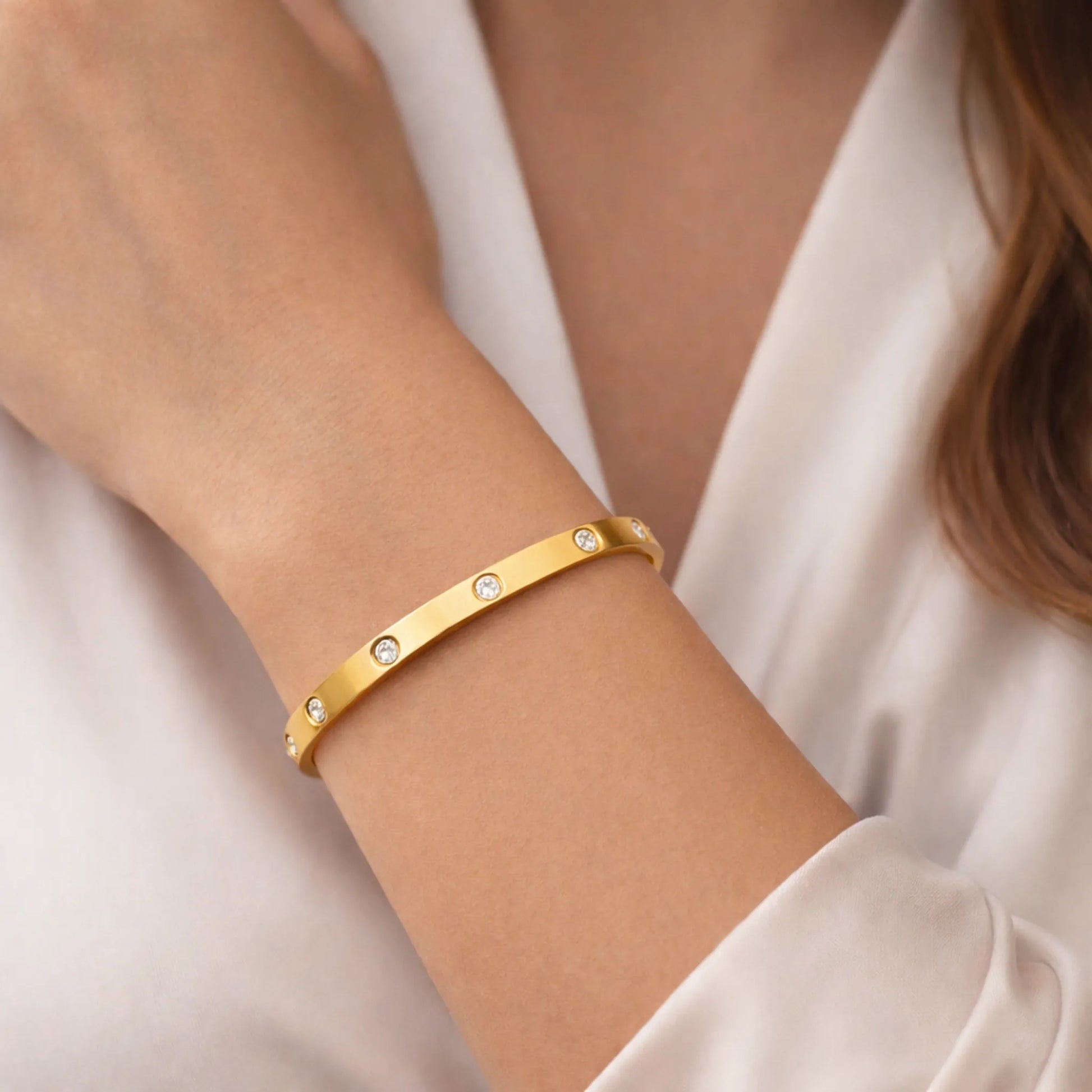 Gold bracelet with small diamonds on a person's wrist against a white background