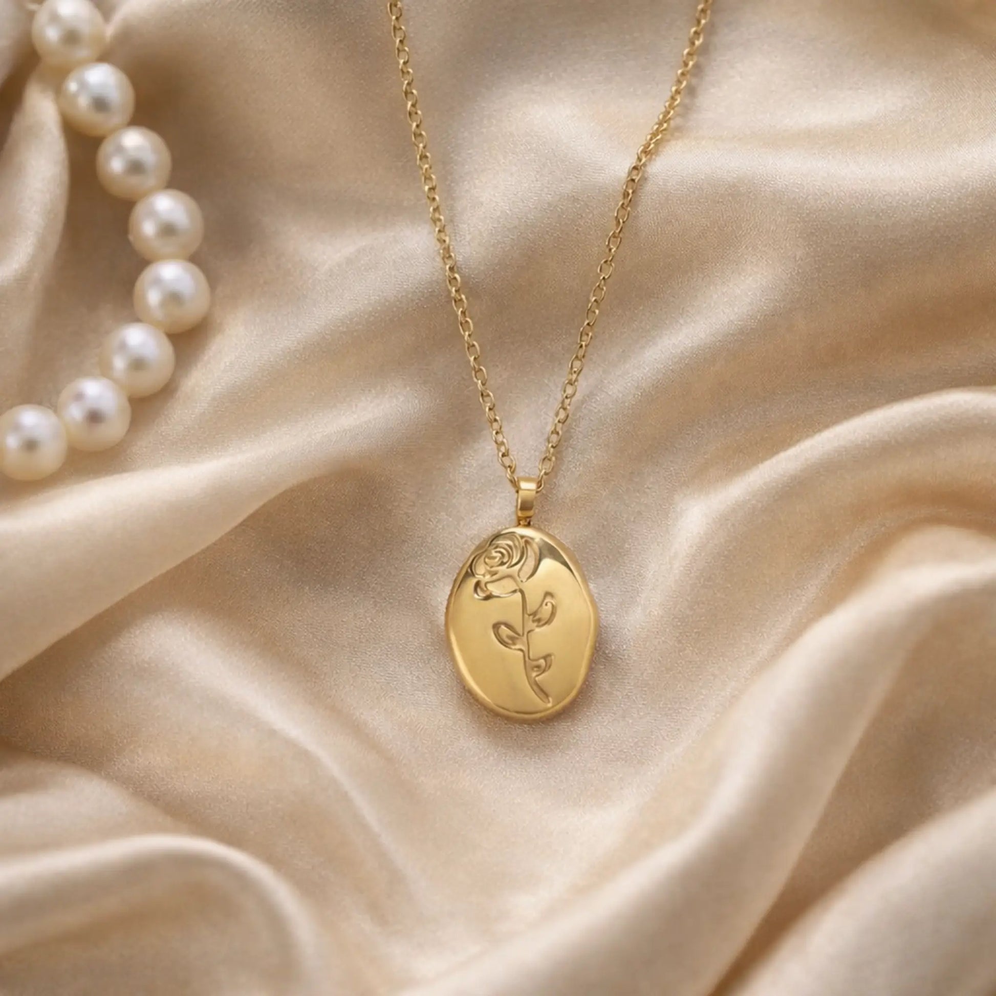 Gold rose pendant necklace styled on satin fabric with pearls, elegant jewelry aesthetic