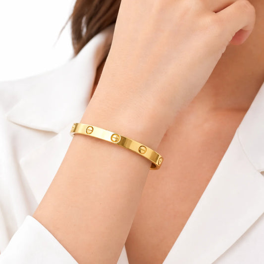 Gold bracelet with screw engraving worn on a wrist against a white background