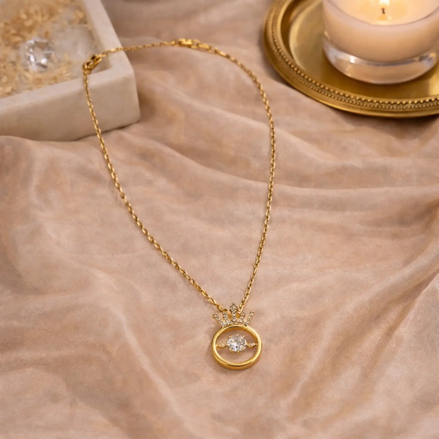 Gold crown circle pendant necklace styled in elegant flat lay with soft neutral fabric for premium jewellery presentation
