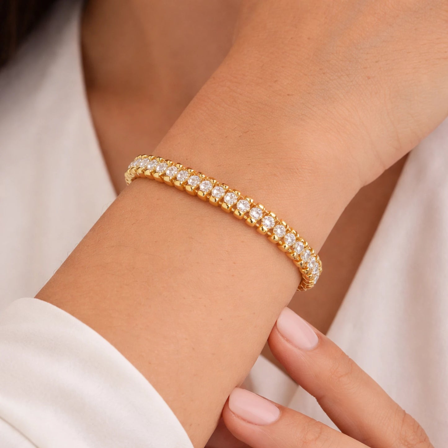 Gold bracelet with clear stones on a wrist against a neutral background