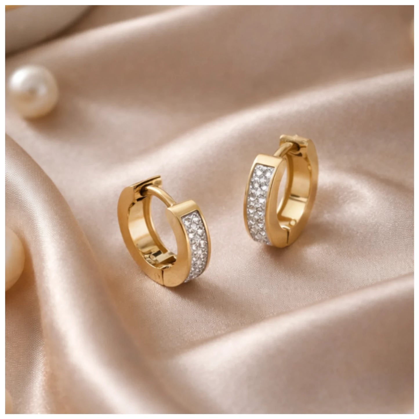 Gold hoop earrings with embedded stones on a satin surface