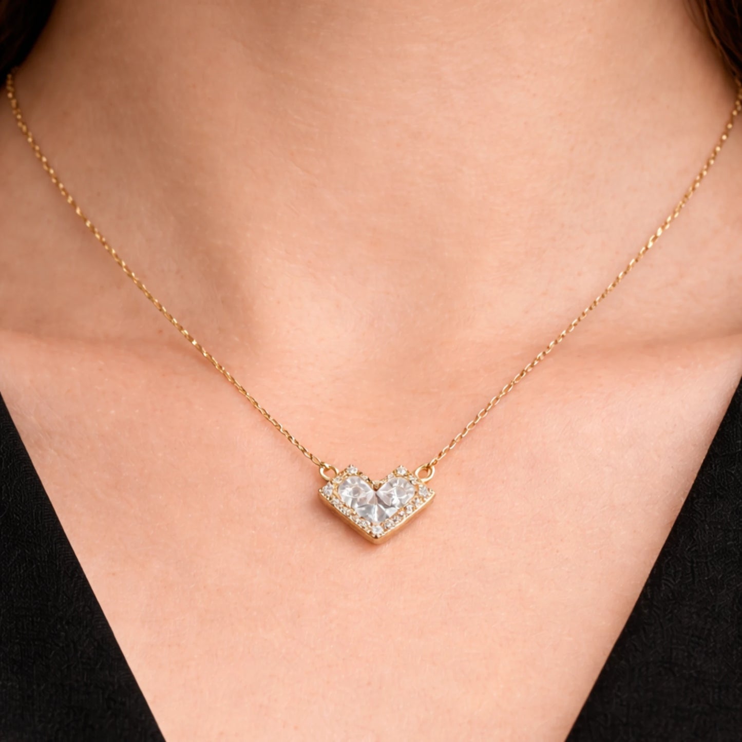 Gold necklace with a heart-shaped diamond pendant on a person wearing a black top.