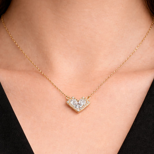 Gold necklace with a heart-shaped diamond pendant on a person wearing a black top.