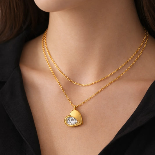 Gold heart-shaped necklace with a diamond on a person wearing a black top.