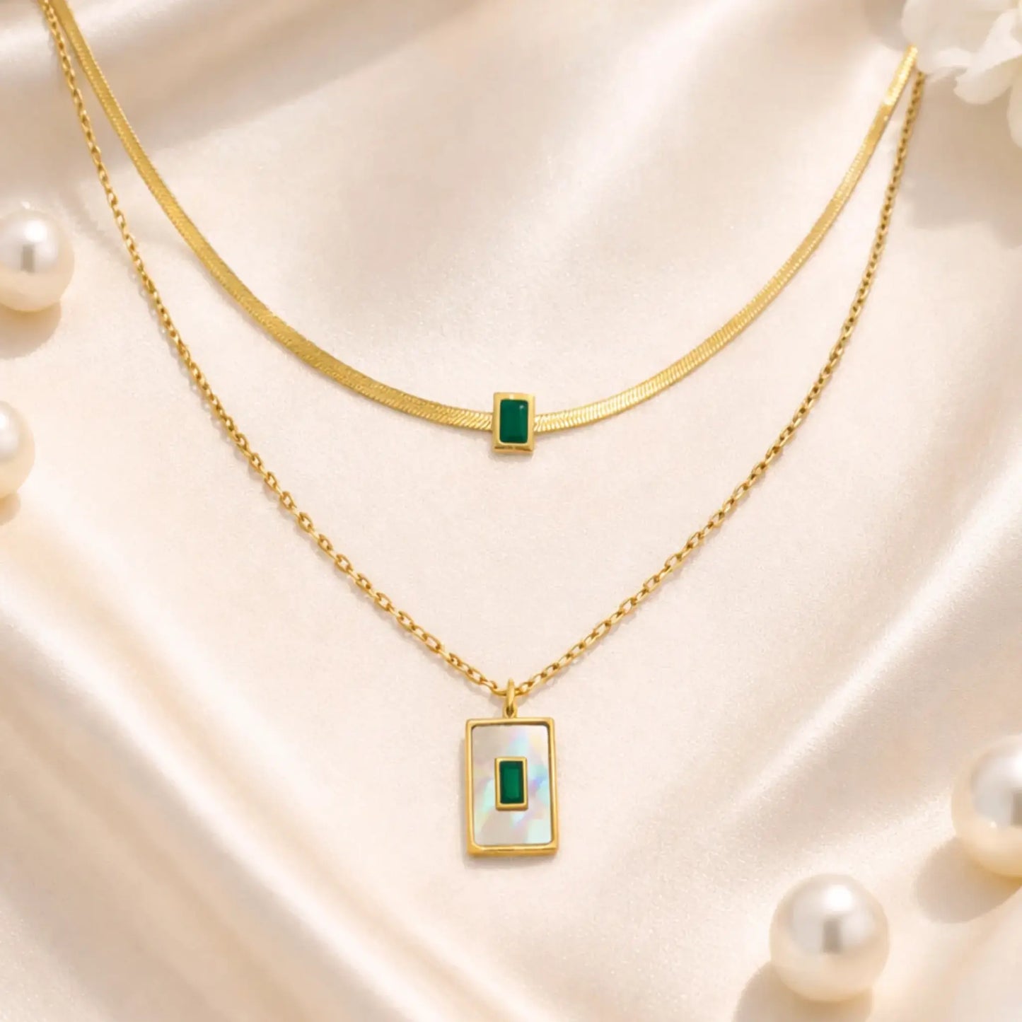 Elegant layered gold necklace with green stone styled on satin fabric with pearls