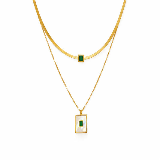 Gold layered necklace with emerald green stone pendant, cropped close-up on white background