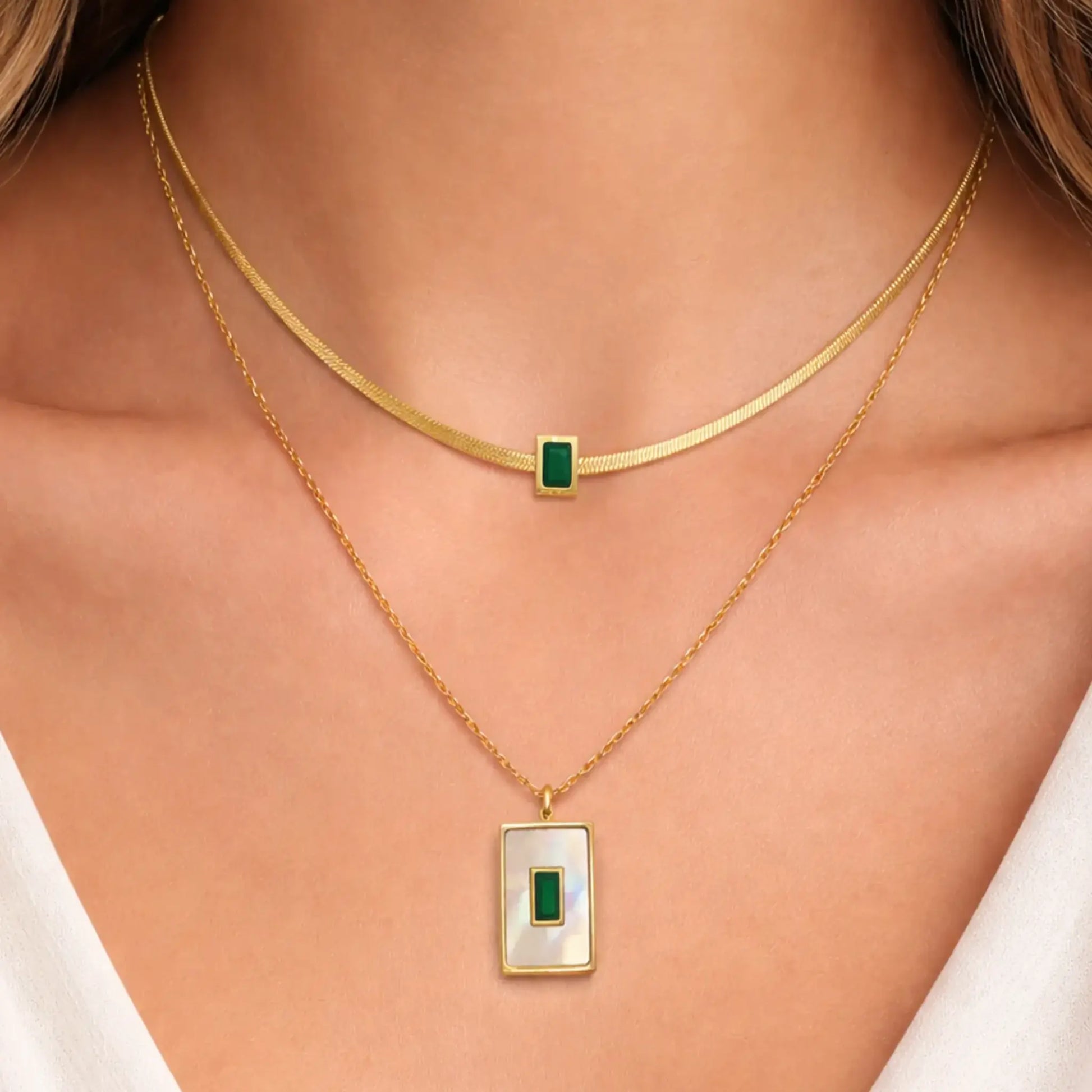 Gold necklaces with green and white pendants on a person's neck