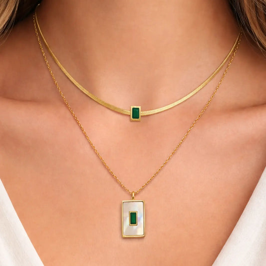 Gold necklaces with green and white pendants on a person's neck