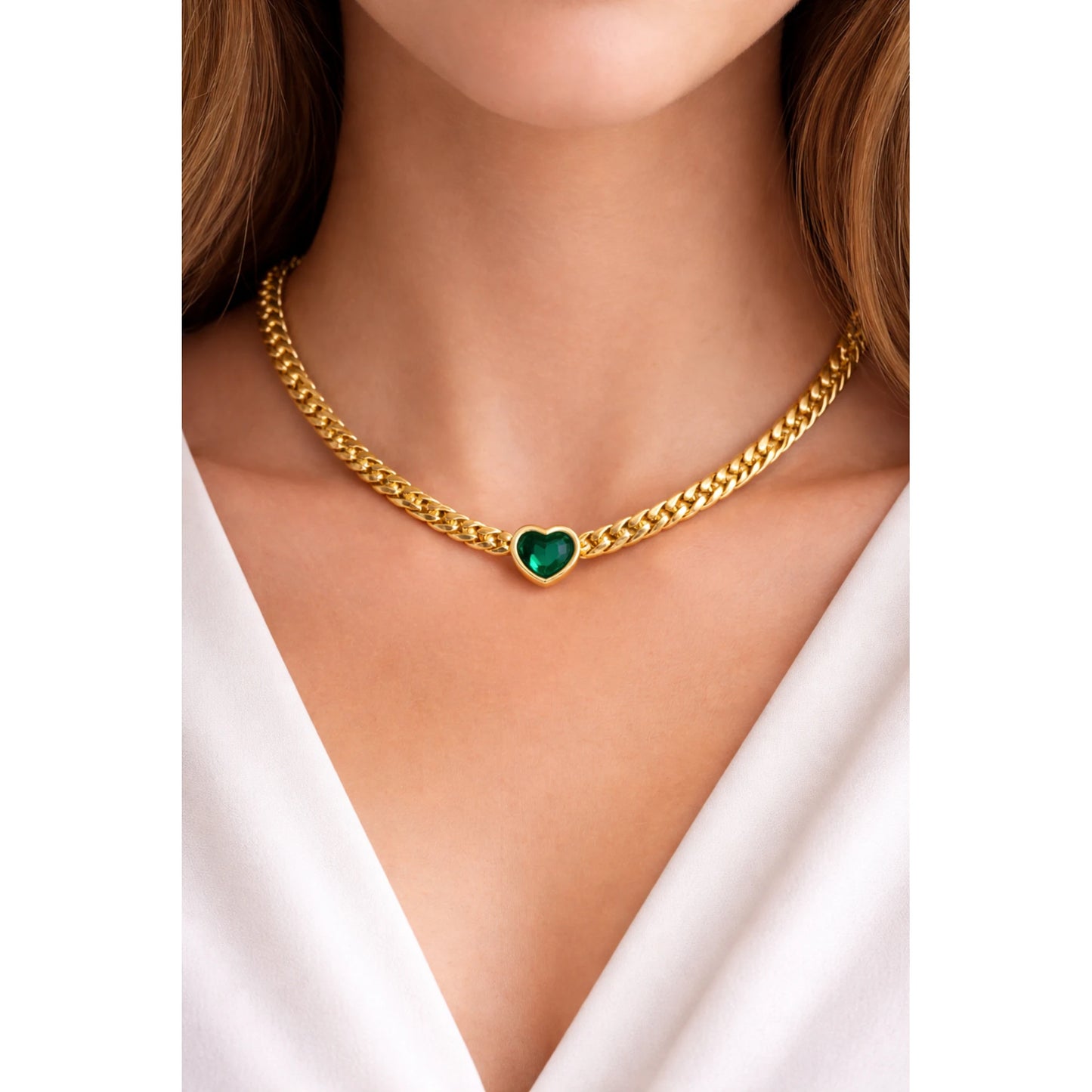 Gold chain necklace with a heart-shaped green gemstone on a model wearing a white top.