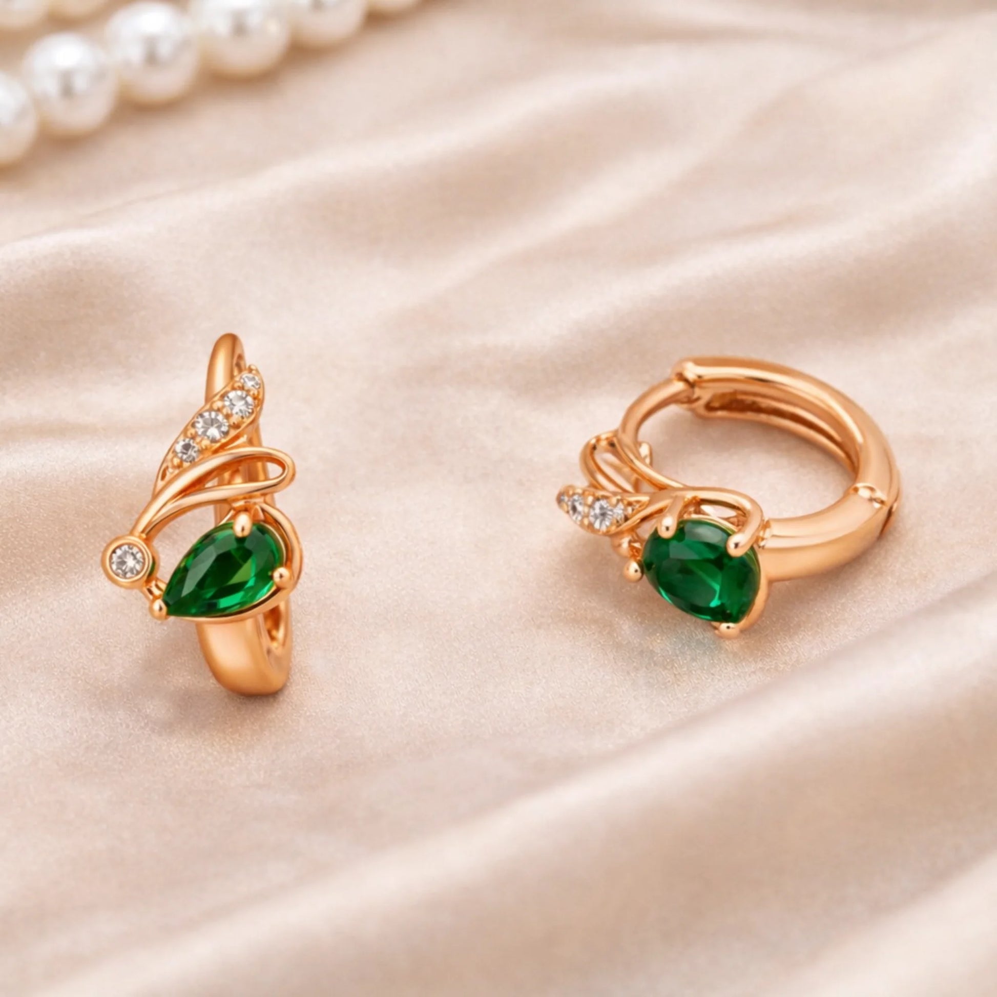 Rose gold huggie earrings with green gemstone styled on satin fabric with pearls for luxury look