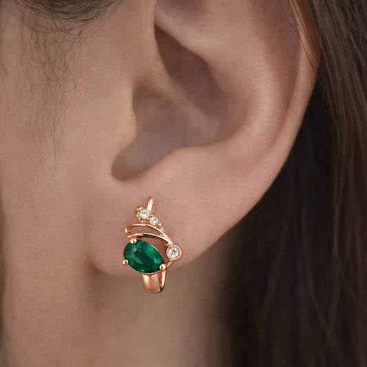 Rose gold huggie hoop earrings with green stone and diamonds worn on ear close-up view