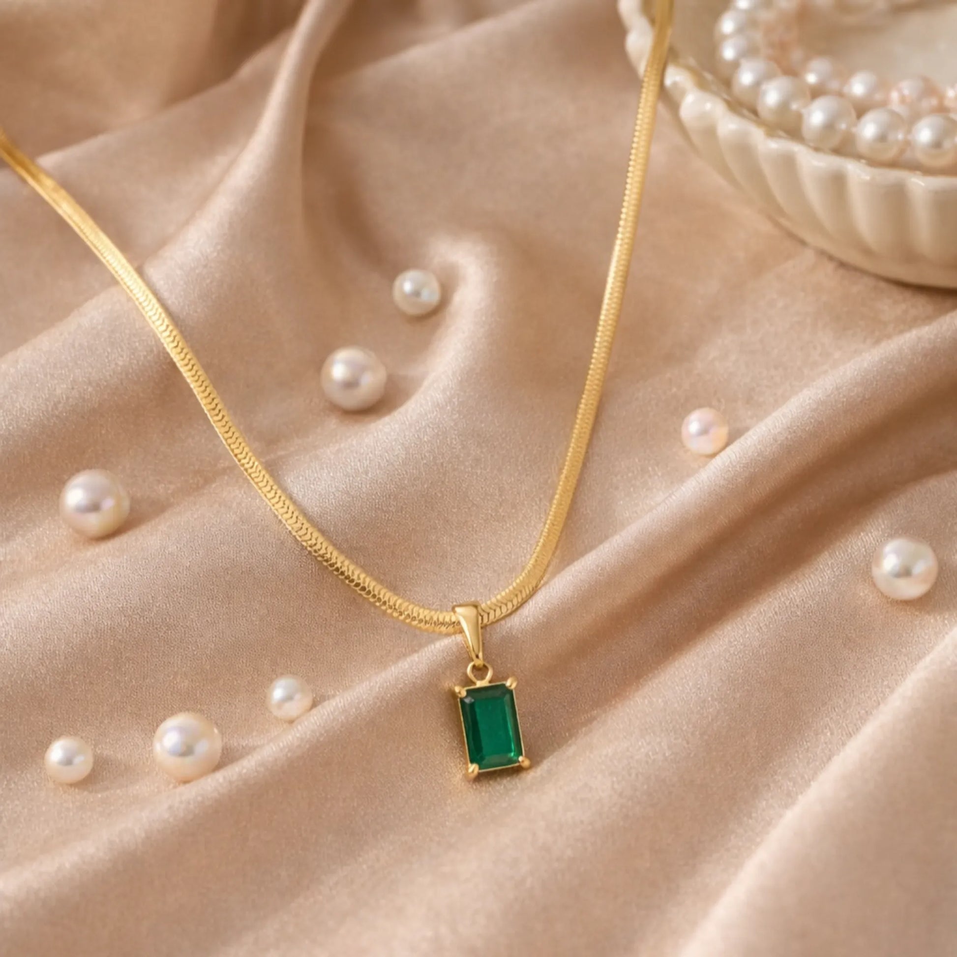 Gold necklace with a green pendant on a beige fabric background