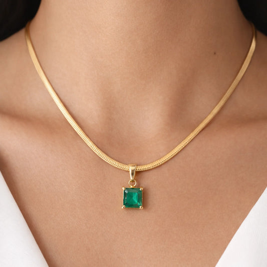 Gold necklace with a green gemstone pendant on a person wearing a white top.
