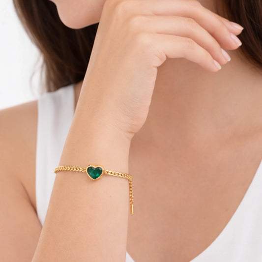 Gold bracelet with a green heart charm on a person's wrist against a white background