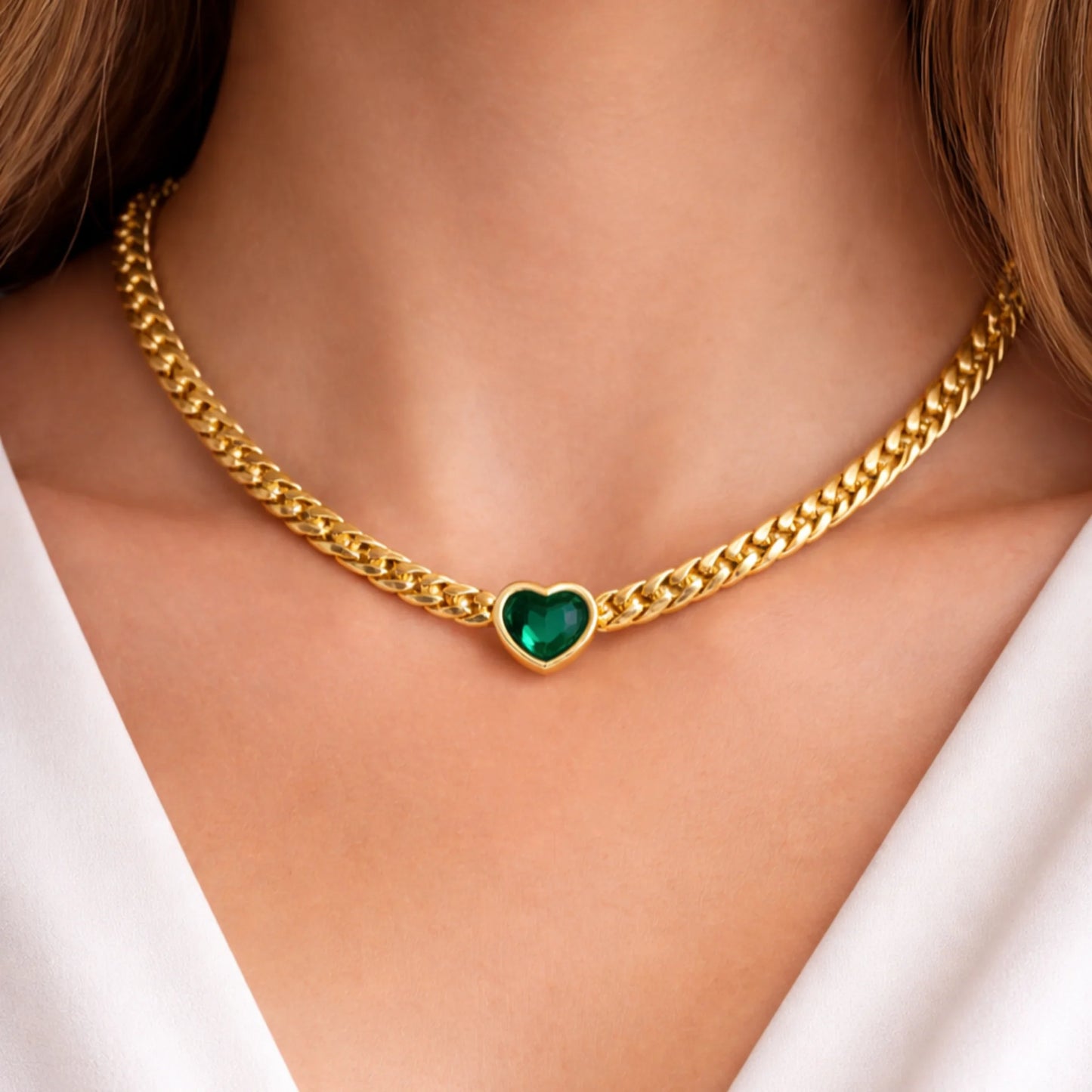 Gold chain necklace with a heart-shaped green gemstone on a person wearing a white top.
