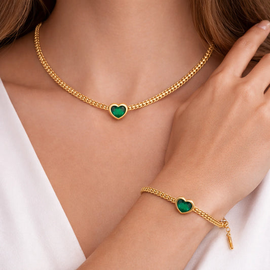 Gold necklace and bracelet with green heart-shaped charms on a person wearing a white top.