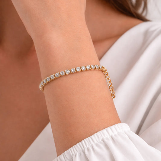 Gold bracelet with clear stones on a wrist against a neutral background