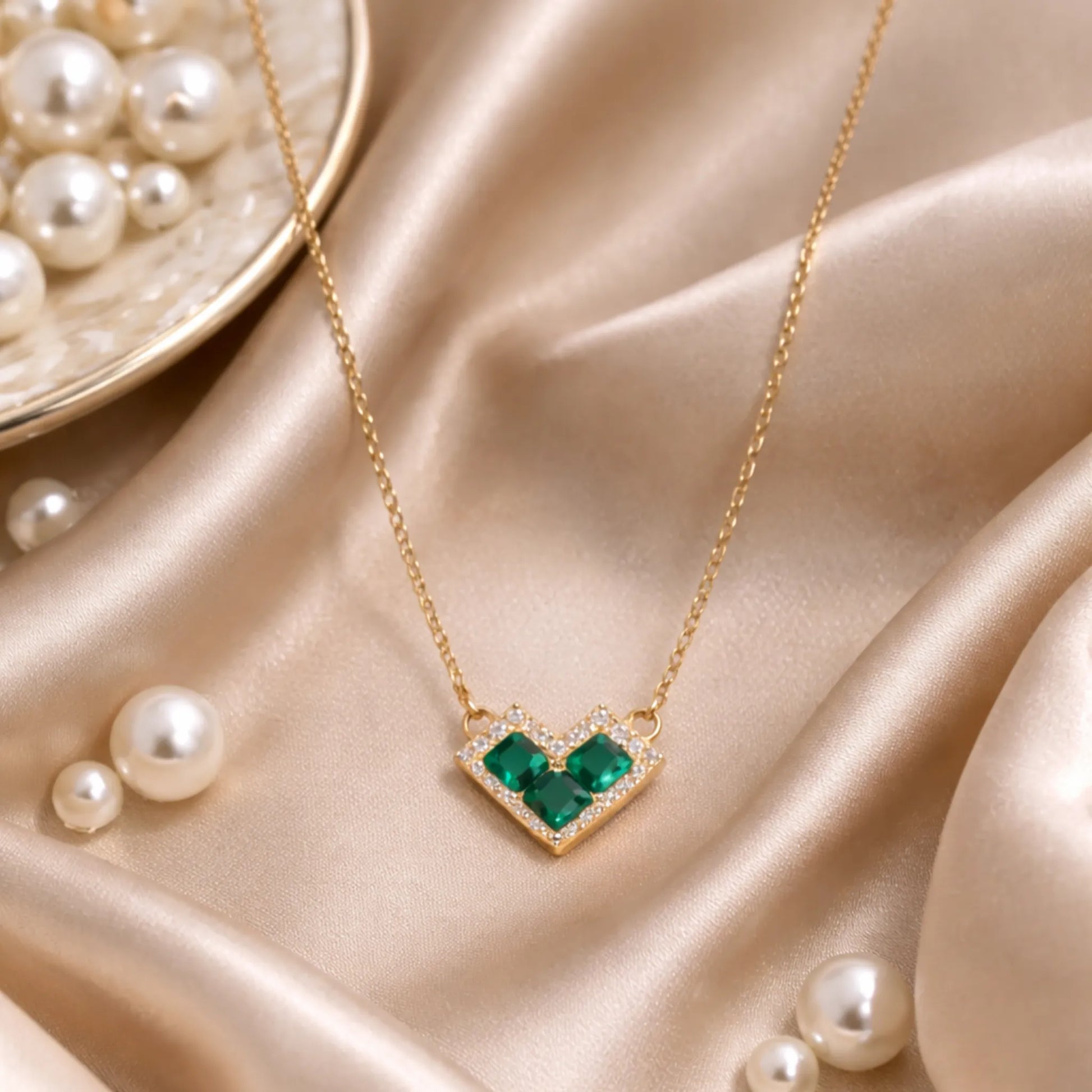 Yubiraa gold heart pendant necklace styled on satin fabric with pearls in luxury flat lay aesthetic