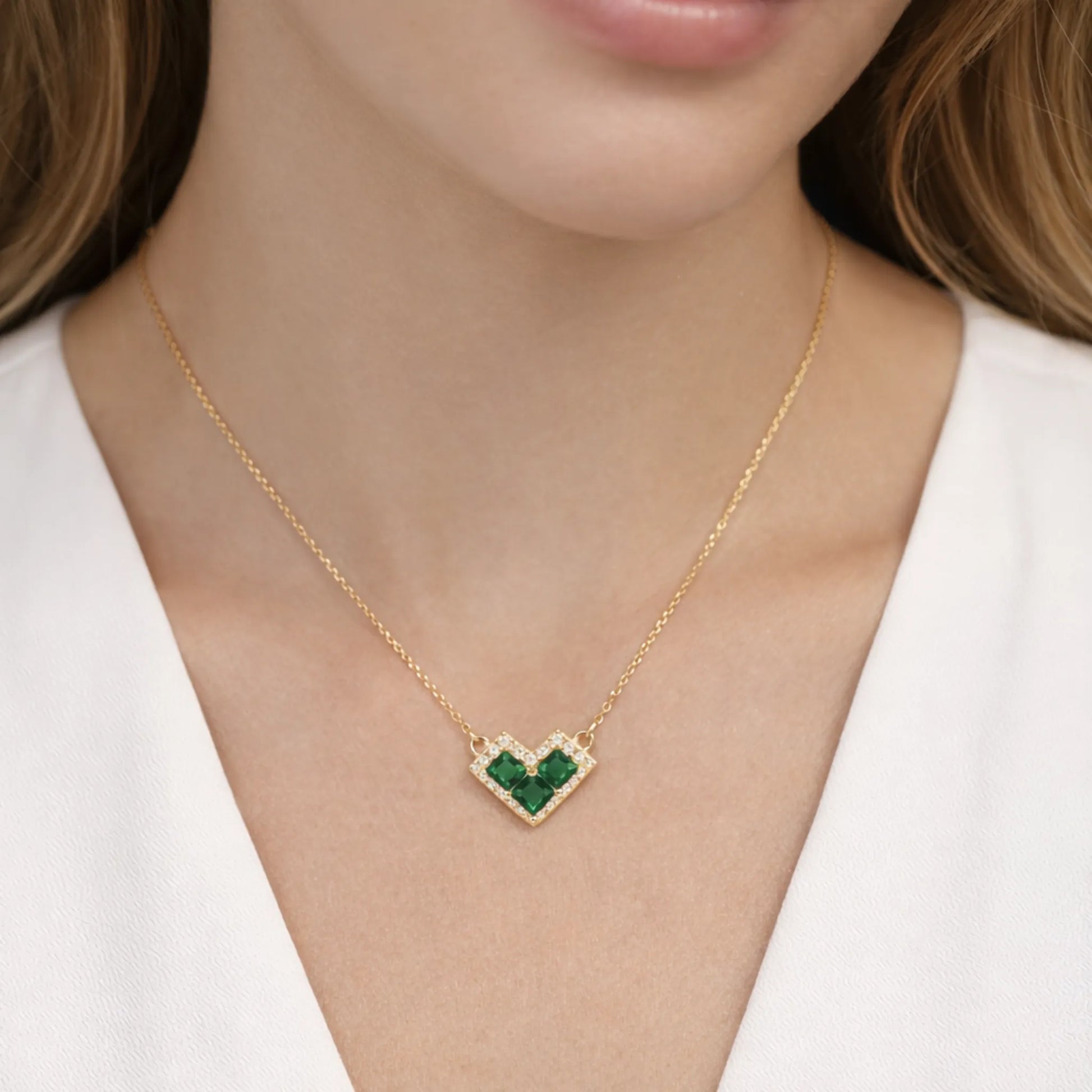 Gold necklace with a green heart-shaped pendant on a person wearing a white top.