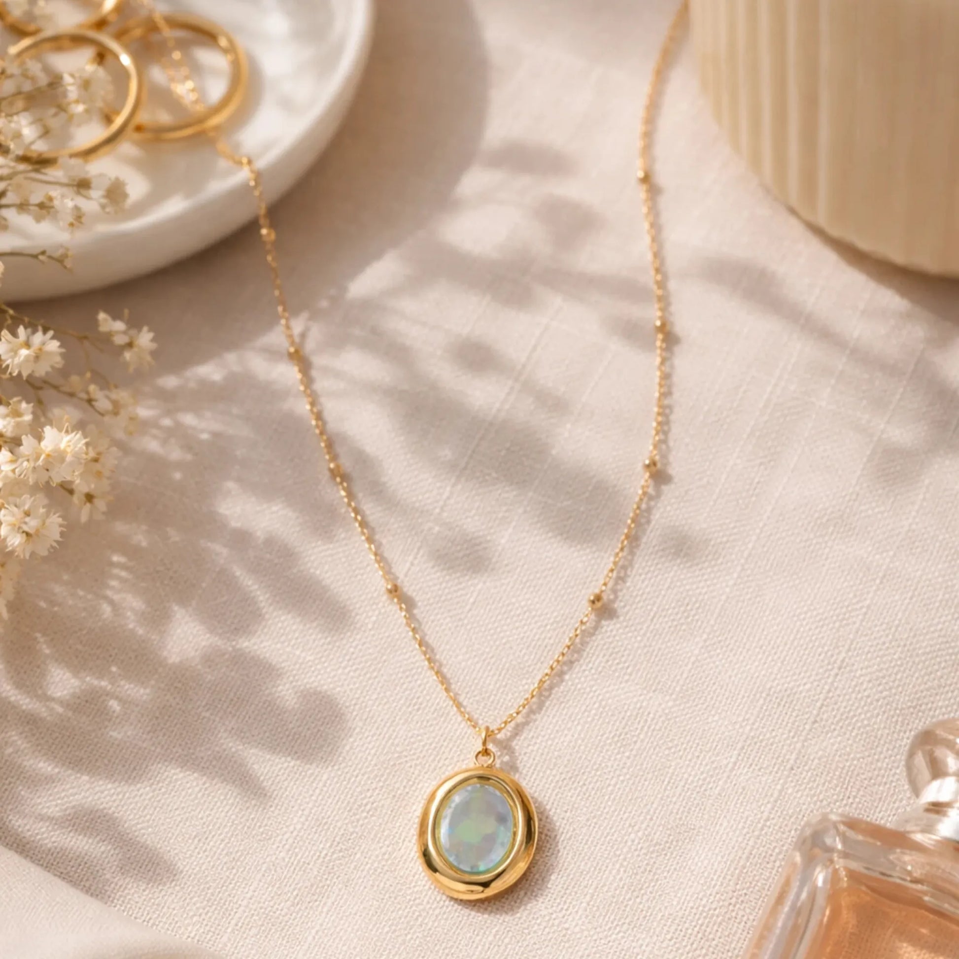 Gold oval opal pendant necklace styled in soft neutral flat lay with elegant lifestyle props
