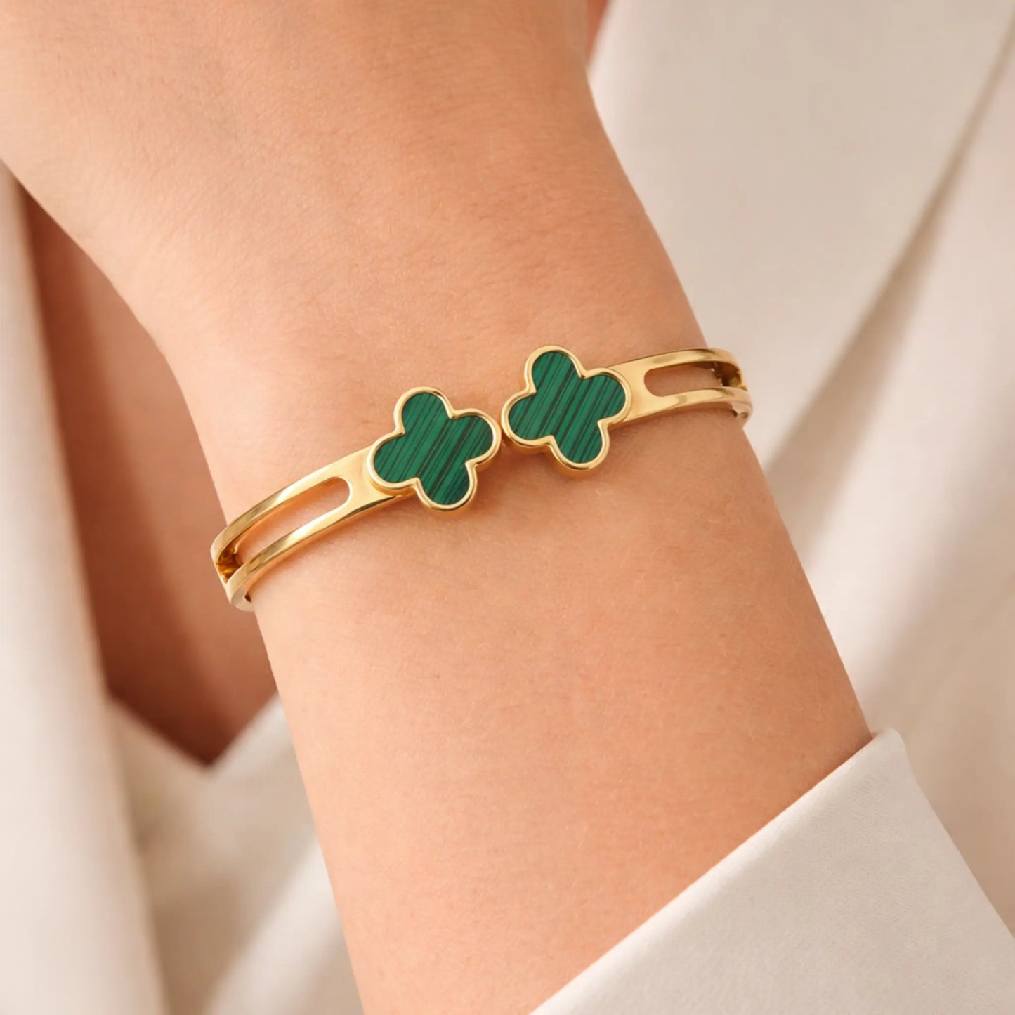 Gold bracelet with green clover-shaped charms on a person's wrist.