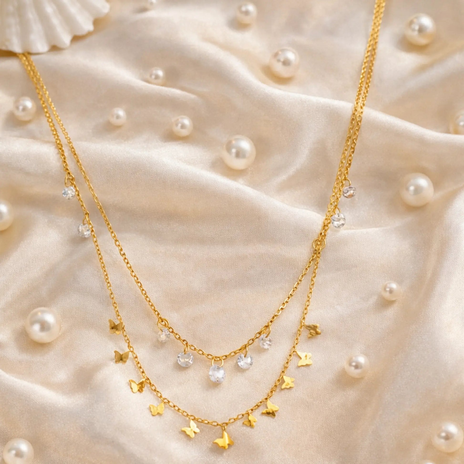 Gold butterfly layered necklace with crystal charms styled on satin fabric with pearls