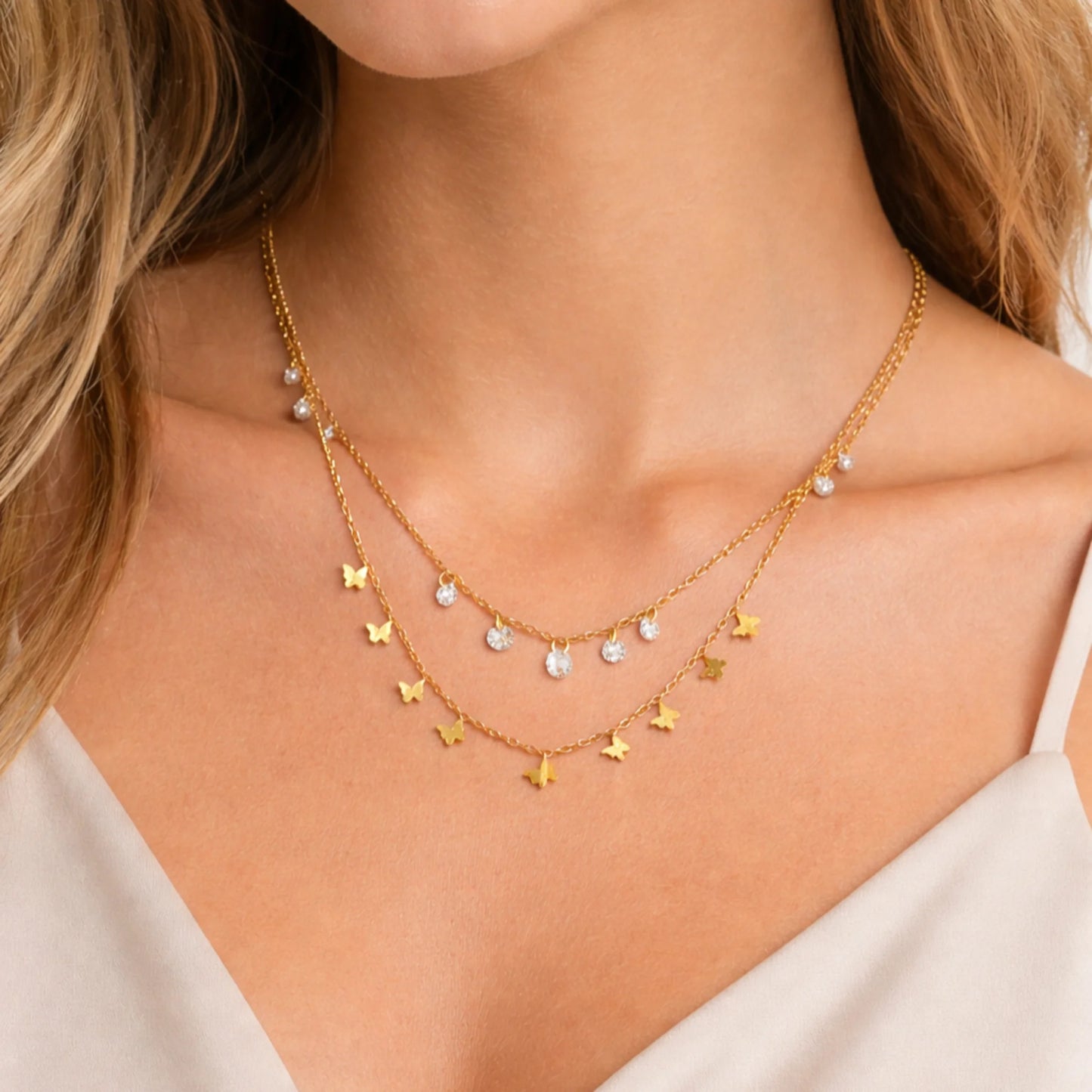 Woman wearing layered gold butterfly charm necklace with crystal drop detailing