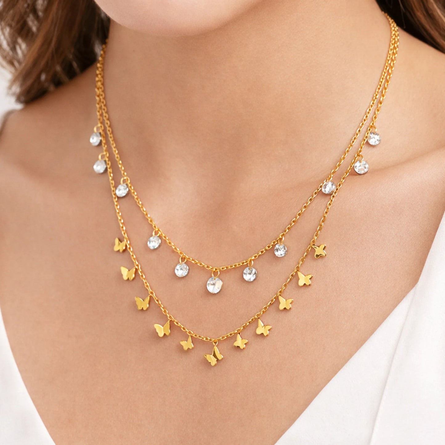 Gold necklace with butterfly and crystal pendants on a person wearing a white top.
