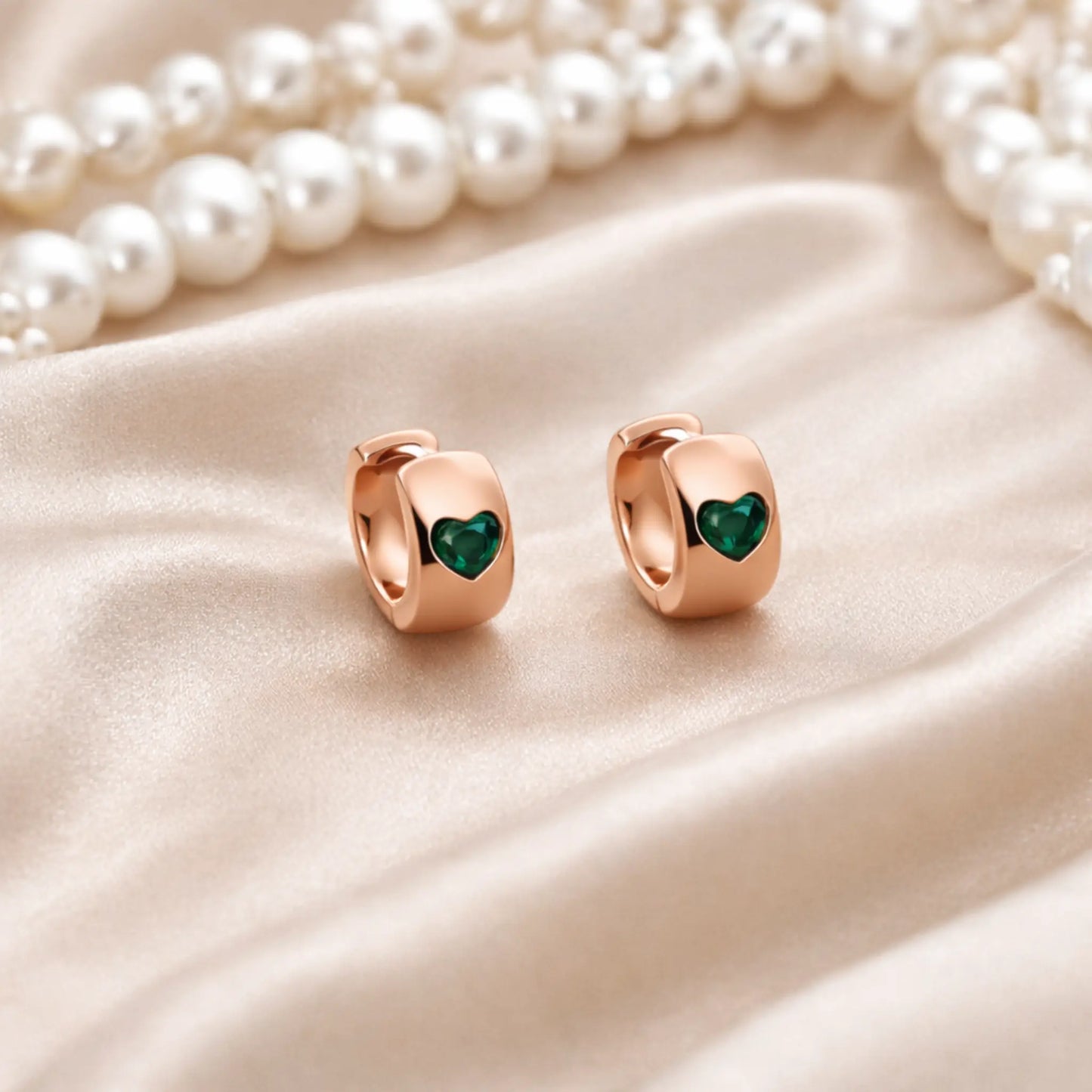 Anti tarnish gold plated heart hoop earrings with green heart detail displayed on satin fabric with pearls
