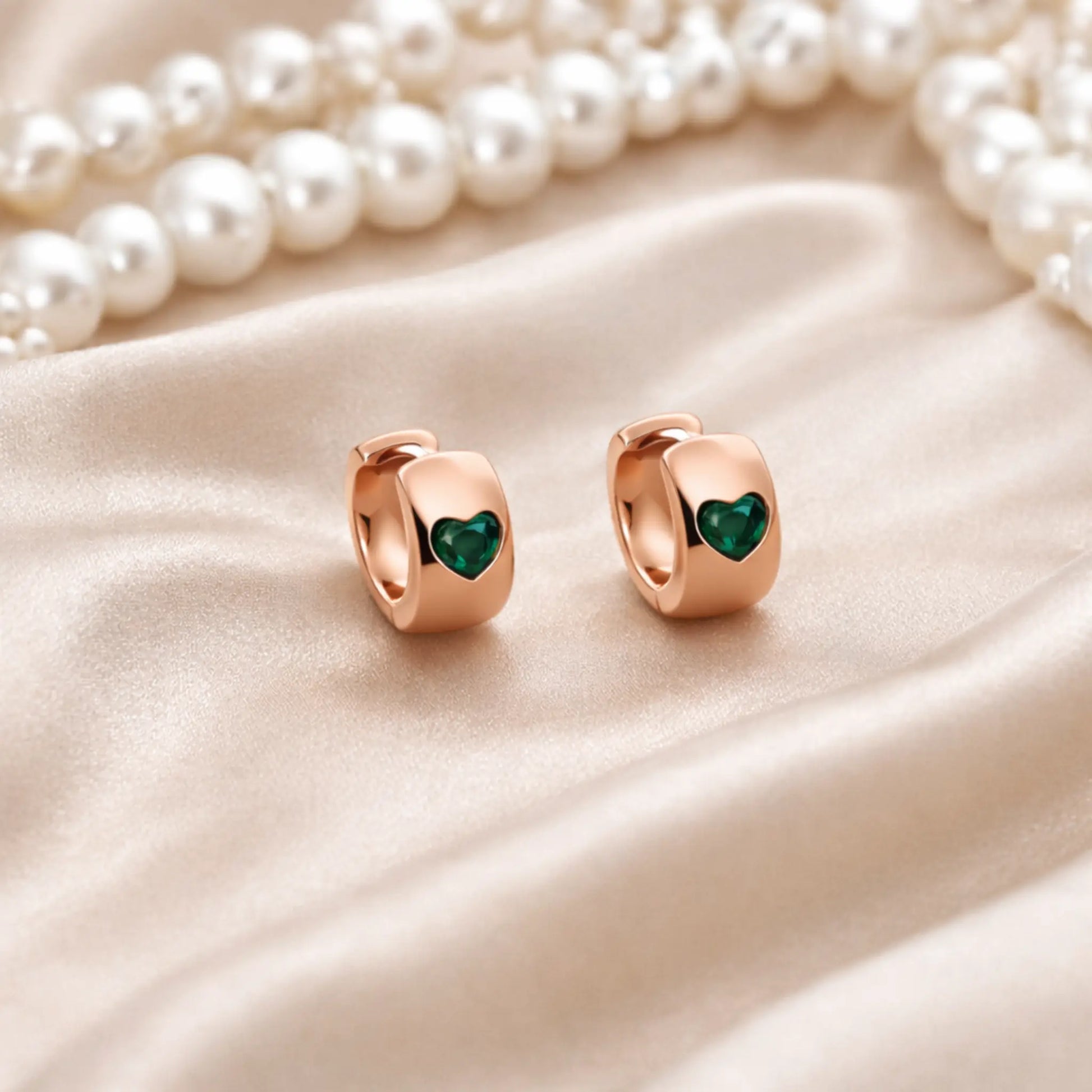 Anti tarnish gold plated heart hoop earrings with green heart detail displayed on satin fabric with pearls