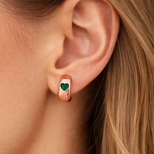 Close-up of an ear wearing a rose gold hoop earring with a green heart charm.