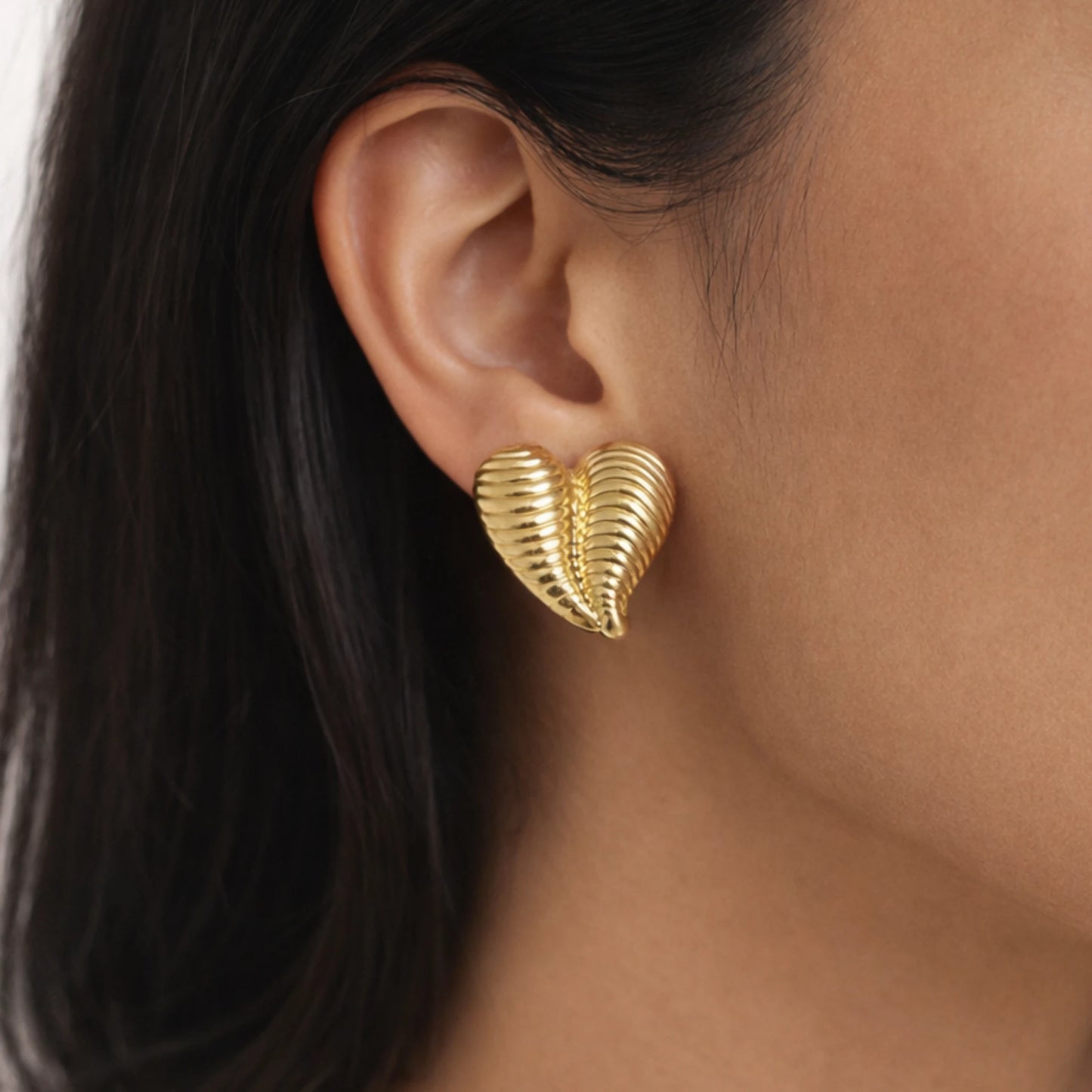 Gold leaf-shaped earring worn by a person with dark hair.